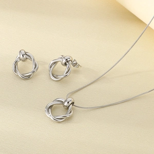 Close-up of polished silver twisted knot earrings and snake chain necklace on beige fabric