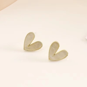 Macro shot of gold-plated heart stud earrings with white mother of pearl inlay texture