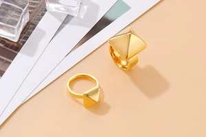 Macro shot of geometric gold pyramid rings on a warm beige background with clear ice cubes