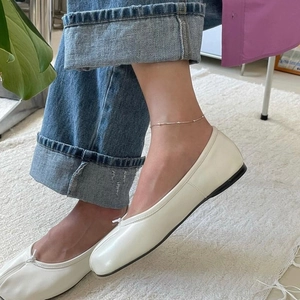 Close-up of a minimalist silver beaded anklet worn with white ballet flats and jeans