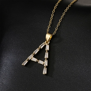 Detail of gold-plated 18K letter A pendant with baguette-cut zircon on black leather