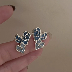 Irregular heart earrings with blue enamel and gold trim shown in a natural hand-held view