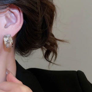 Detailed view of silver C-shaped hoop earrings with irregular wrinkled texture on a model