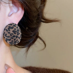 Macro shot of flocked leopard print oval stud earrings worn on model for daily style
