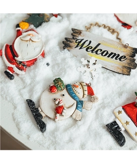 Close-up of resin Christmas ornaments featuring Santa Claus, Snowman and Welcome sign on snow