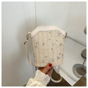 Détail du sac seau en paille avec broderie florale verte et bandoulière en cuir