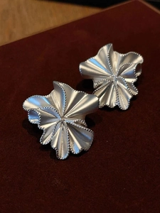 Detailed macro view of silver pleated ruffle floral earrings with textured matte finish