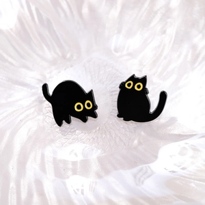Cute black cat stud earrings set with bright yellow eyes on a white ceramic tray