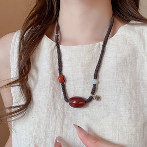 Detail of red agate necklace with hand-woven rope and silver safety charm on a model