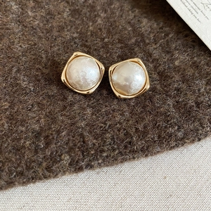 Macro detail of gold-plated square geometric earrings featuring white imitation pearls