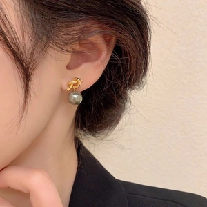 Close-up of elegant gold knot earring with a grey pearl pendant on a model's ear