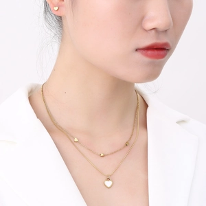 Detailed view of a gold double-layer heart necklace and matching earrings on a female model