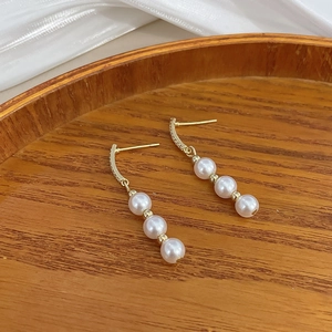 Detailed macro view of gold tassel earrings with three pearls and sparkling zircon accents