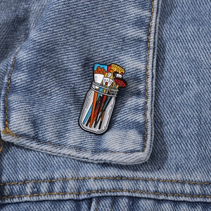 Artistic paintbrush enamel pin badge on blue denim fabric background closeup