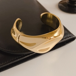 Macro shot of wide gold pleated cuff bracelet on premium black leather background