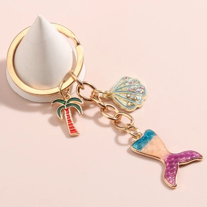 Detail of mermaid tail keychain with palm tree and shell charms on gold ring
