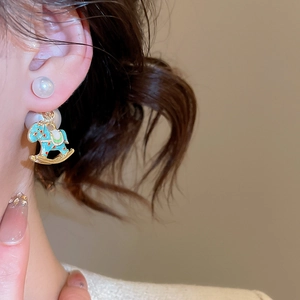 Detail view of gold earrings with white pearl and blue enamel rocking horse pendant