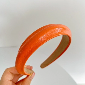 Close-up of hand holding an orange faux leather padded headband with smooth texture