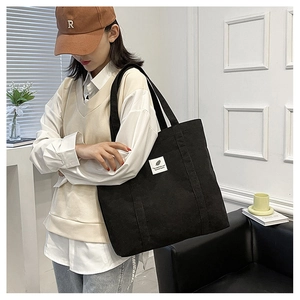 Detail of a large black corduroy tote bag with a white minimalist label on a model