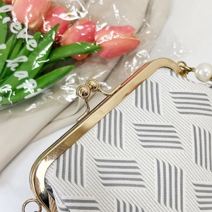 Detail of shell-shaped clutch bag with woven texture, pearl handle and gold clasp