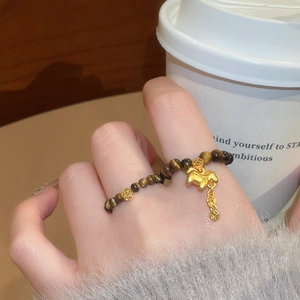 Detail of tiger eye bead ring with golden horse charm and coin tassel on finger