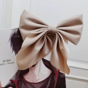 Detail of a large beige matte fabric bow hair clip with soft drape and center knot detail