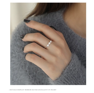 Macro shot of silver ring with three zircon flowers worn against a soft grey sweater