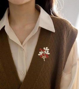 Detail of camellia flower brooch with red enamel and pearls on brown knit vest
