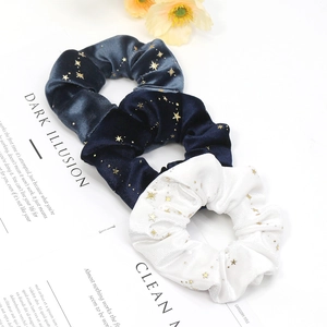 Three elegant gold star velvet scrunchies in navy blue and white on a magazine background
