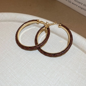 Detail of large brown braided leather hoop earrings with gold-tone metal base accents