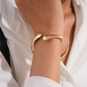 Detail of a minimalist gold open cuff bracelet with teardrop ends on a wrist