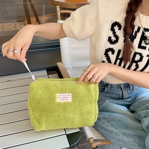 Fuzzy green plush makeup bag with inspirational label held in a bright outdoor setting