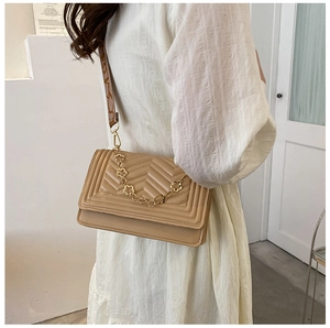 Detail of khaki chevron quilted crossbody bag with decorative gold clover chain