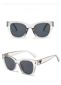 Detail views of oversized square sunglasses with a heart emblem on the transparent grey temple