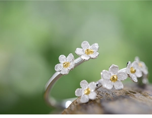 Macro shot of silver S925 forget-me-not flower ring with gold centers on wood