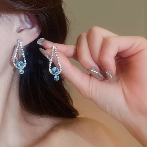 Close-up of silver drop earrings featuring blue gemstones and sparkling crystals