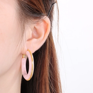 Macro detail of a pink resin earring with a gold stainless steel rim on a model