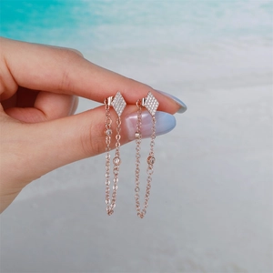 Close-up of rose gold tassel earrings with colorful zircons on a beach background