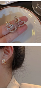 Detalle de pendientes de corazón con diamantes y aros con flores de esmalte blanco