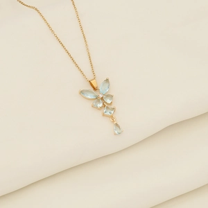 Detailed view of golden butterfly necklace with light blue stones on beige fabric