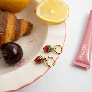 Macro shot of 18K gold plated strawberry drop earrings on a decorative white dish