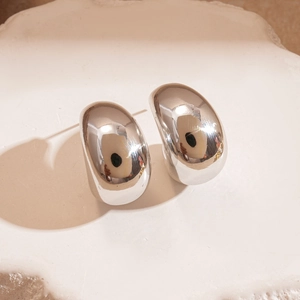 Macro detail of polished silver C-shaped chunky hoop earrings on a stone tray