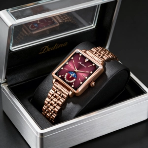 Close-up of a square rose gold watch with red moon phase dial in a luxury silver gift box
