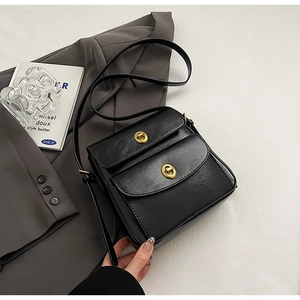 Close-up of black PU leather flap bag with gold hardware on a grey suit jacket
