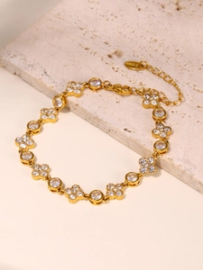 Detailed shot of 18k gold plated clover and zircon bracelet on beige stone