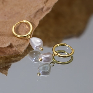 Detailed close-up of gold hoop earrings with irregular white pearl drops on a mirror