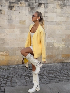 Chic yellow knit cardigan with white mini dress and high boots in an outdoor street style