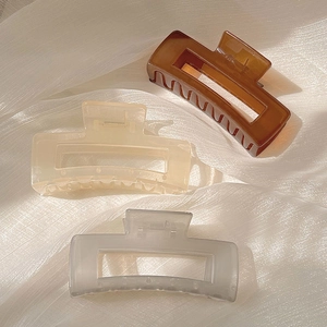 Three large matte square hair claws in amber, beige, and grey on white fabric background
