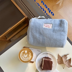 Top view of light blue sherpa fleece cosmetic bag on a cozy cafe table with latte