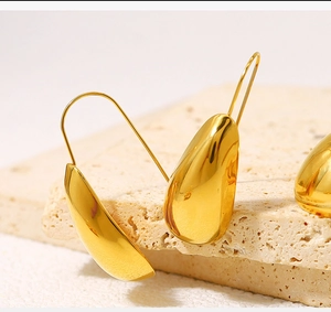 Detailed side view of high-polished 18K gold teardrop earrings on a beige stone base